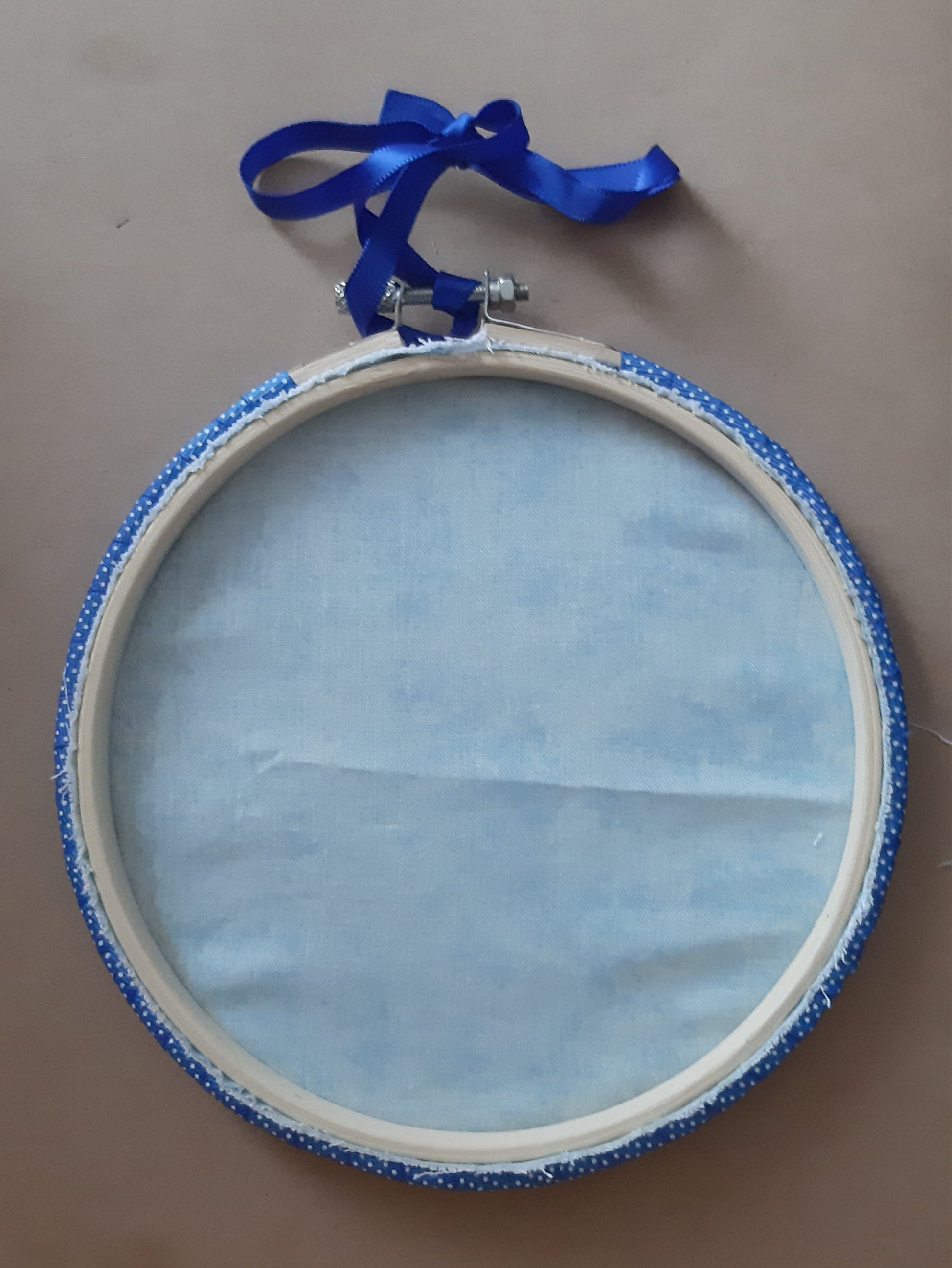 6 inch embroidery hoop is backed in light blue cotton with hoop wrapped in blue ribbon