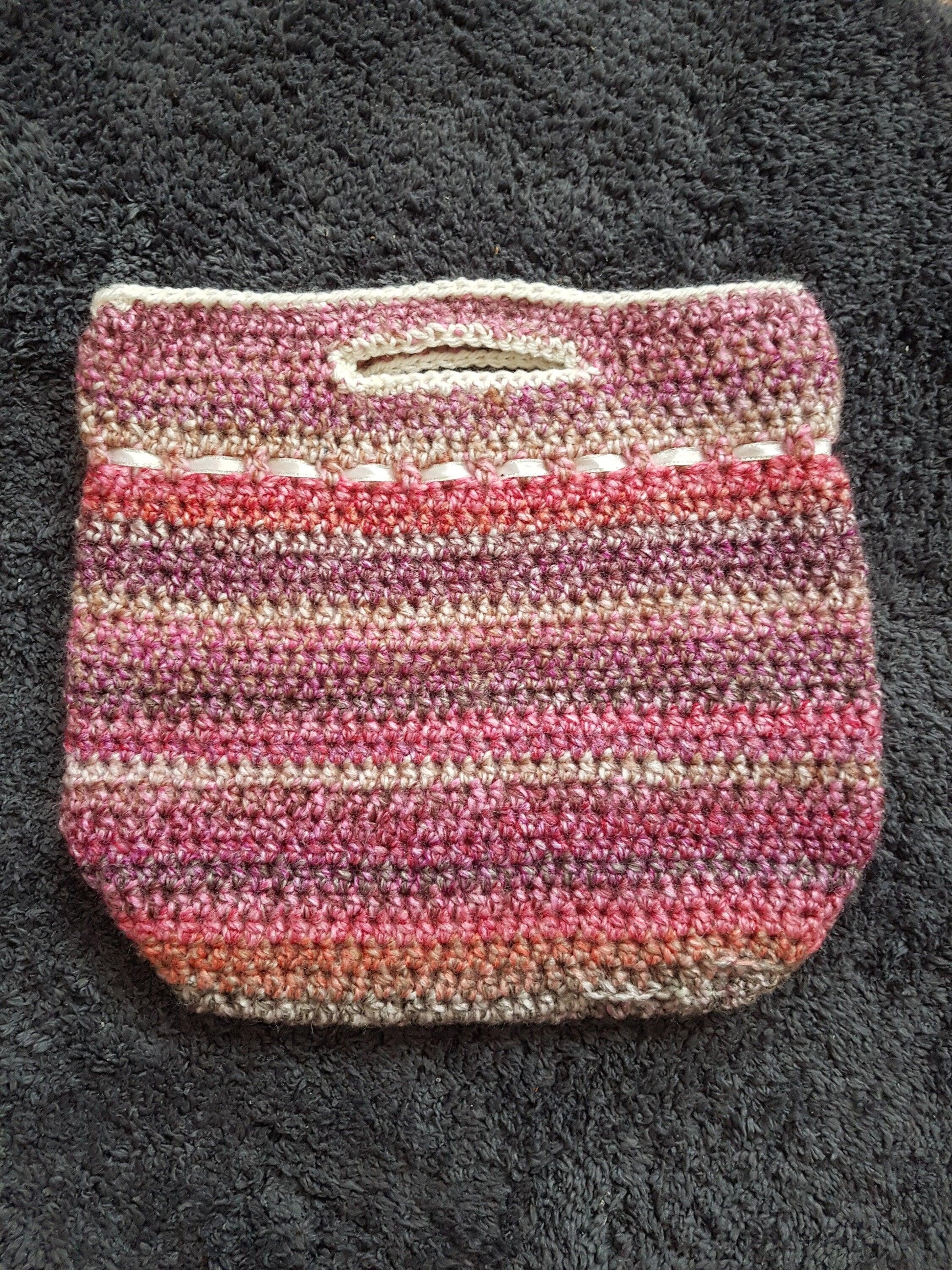 Handmade crochet handbag in mixed pink yarn. Back of the bag shown on floor to show detail