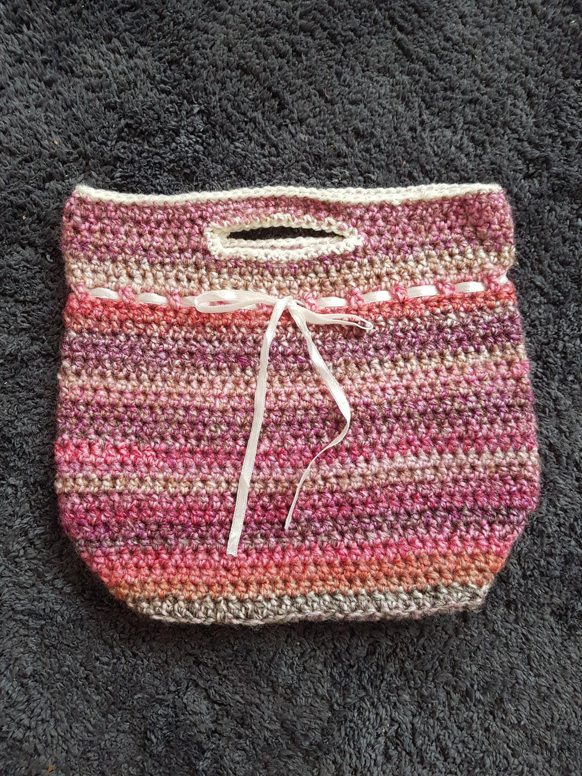 Handmade crochet handbag in mixed pink yarn. Front of the bag shown laid flat on the floor to illustrate detail