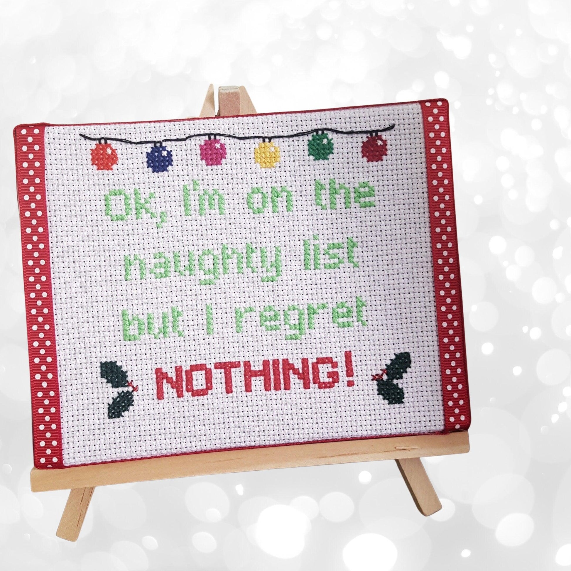 Completed cross still on canvas with easel with the words 'Ok, I'm on the naughty list but I regret nothing!'