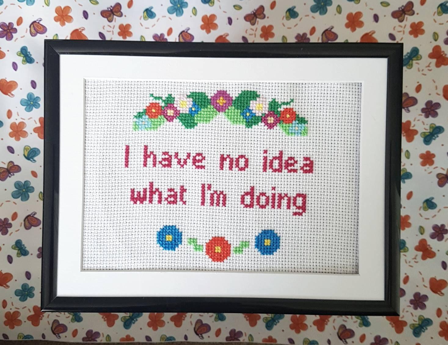 Completed cross stitch from Thistleflat Crafts with the words 'I have no idea what I'm doing' in a floral border. Comes in a black frame with mount