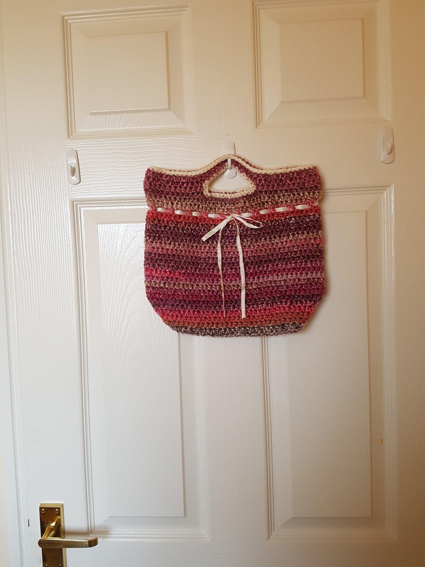 Handmade crochet handbag in mixed pink yarn. Shown hanging on the back of an internal door to demonstrate size