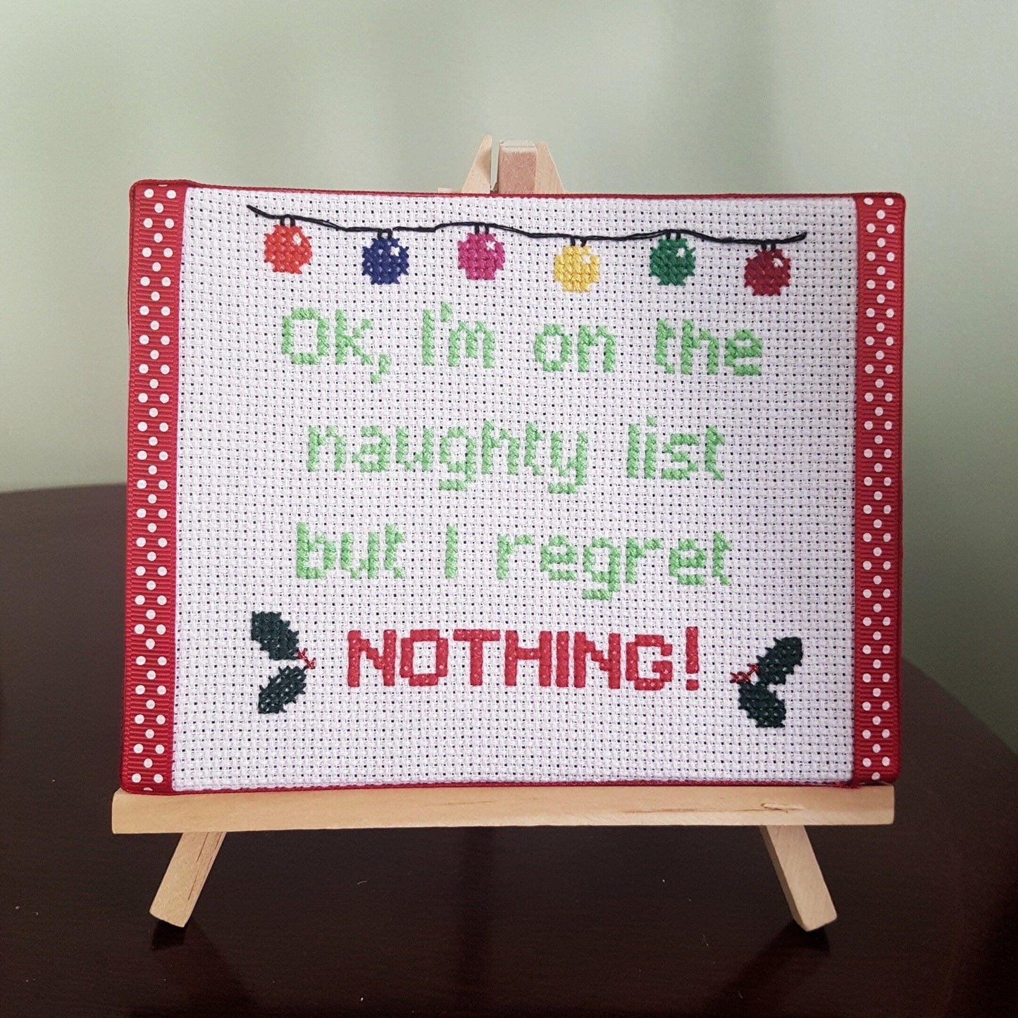 Completed cross still on canvas with easel with the words 'Ok, I'm on the naughty list but I regret nothing!'